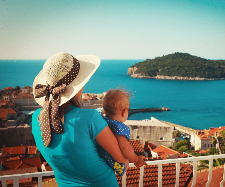 A woman in a blue dress jolding a baby and admiring the vies on her family getaway to Dubrovnik