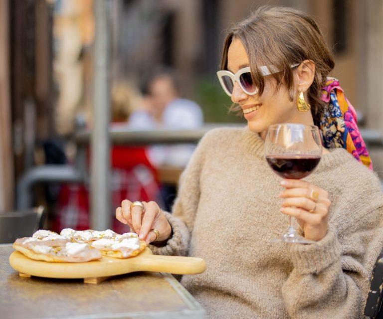A woman is enjoying a local pizza and a glass of wine in Rome