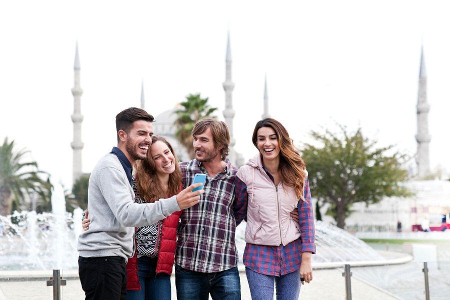 A group of four friends taking a selfie with the grand Blue Mosque on the background, a must-visit place on a weekend break to Turkey