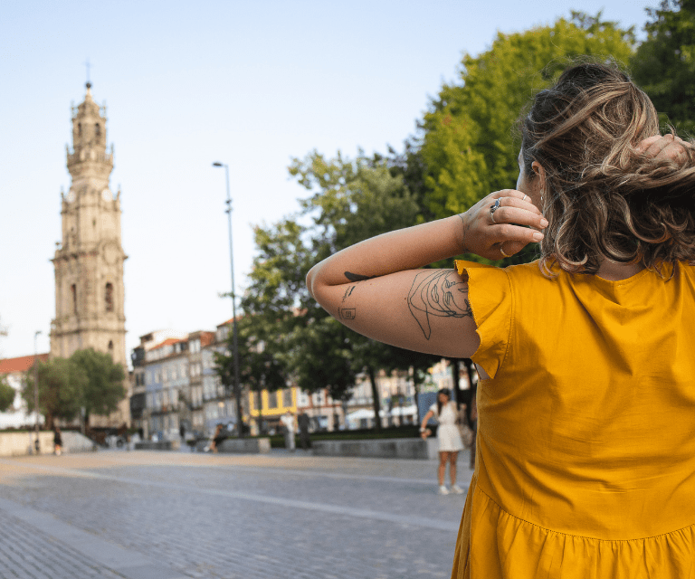 A woman wearing a yeallow dress is admiring the Clérigos Tower, a must-see thing on a Porto weekend break