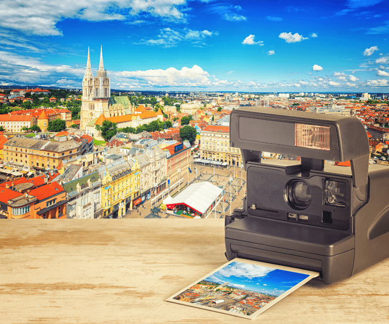 There is an instant camera on the front of the picture, with a bird-eye view of Zagreb lying next to it. On the background you can see the panorama of Zagreb that the picture is taken of