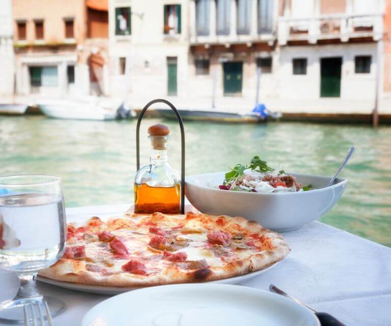 A restaurant table with pizza and salad in a restaurant, offering stunning views over Venice canals