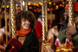 A young woman is enjoying a ride on a carousel and smiling. She is looking at a man next to her who is also having a great time during his christmas break to Munich.