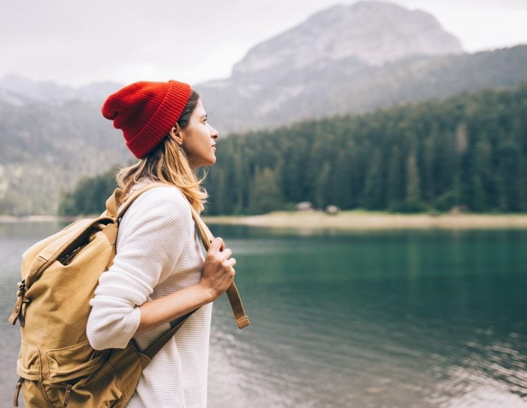 A woman is wearing a red hat, white hoodie and a backpack. She is hiking