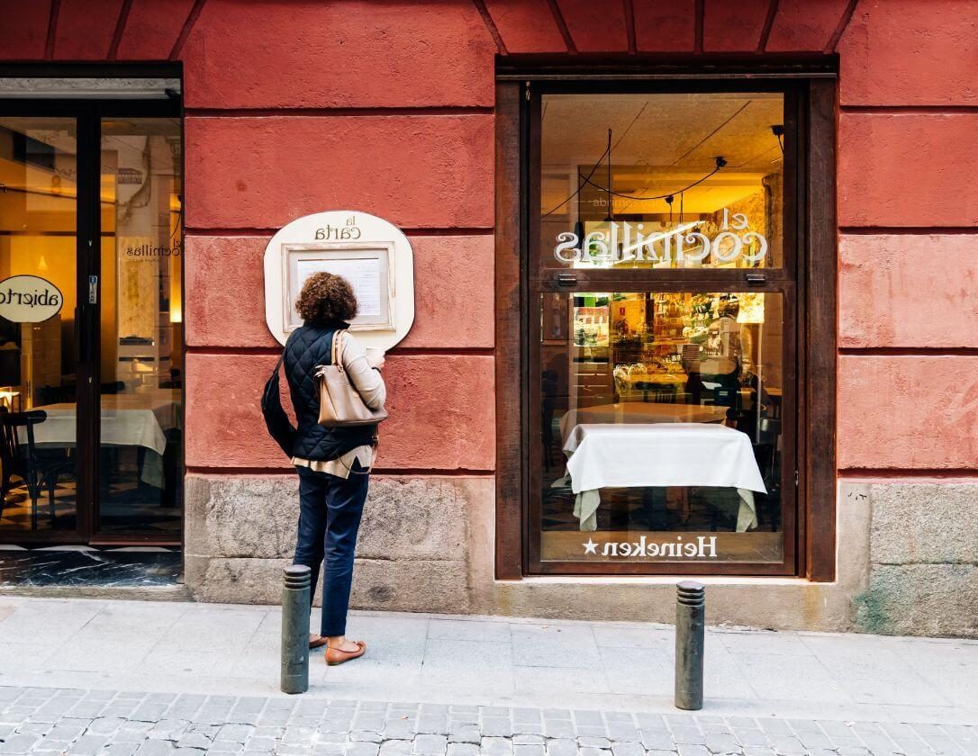 A woman reading the menu outside a cafe in madrid on her solo getaway.